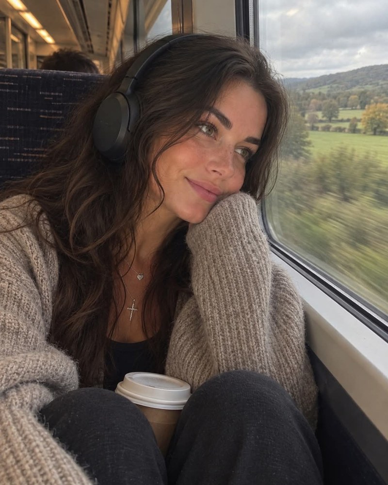 Portrait beside a train window, wearing headphones and a knitted cardigan.